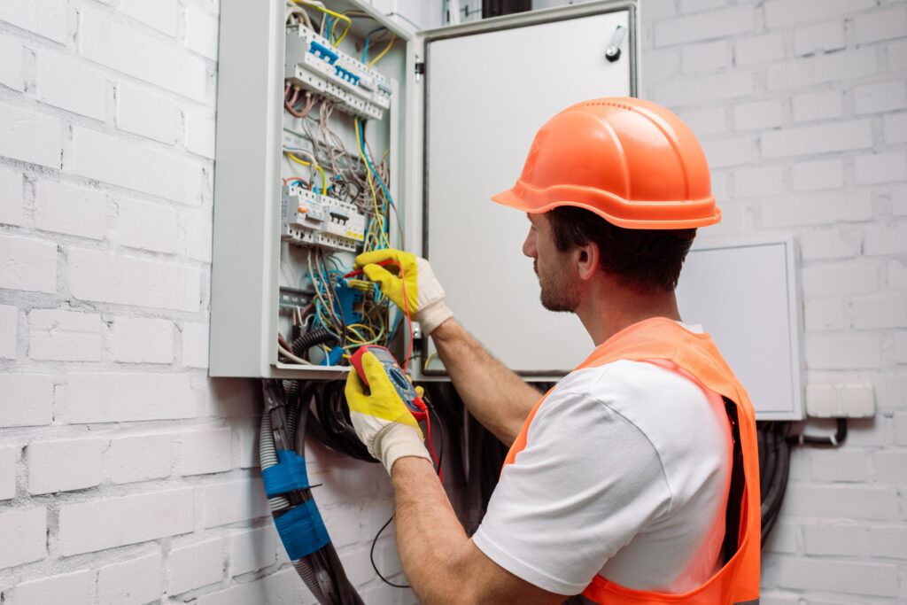 Handsome electrician in hardhat and gloves holding multimeter ne